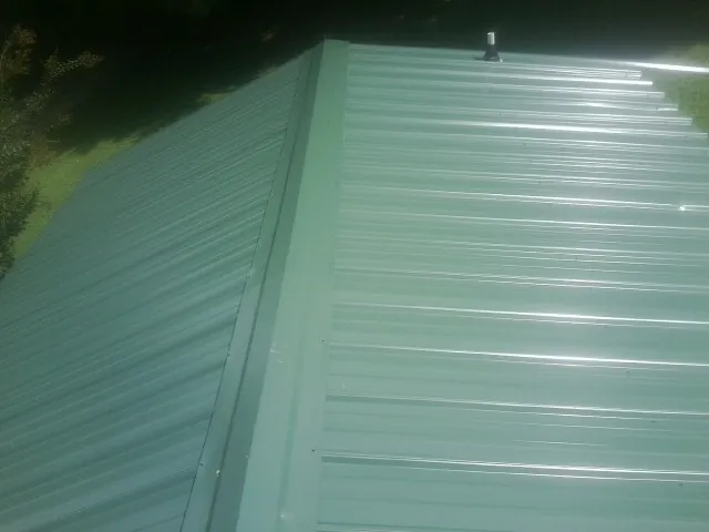 New green metal panels meeting at the ridge of a roof — Flat Roof Repair work by our crew in Lake City