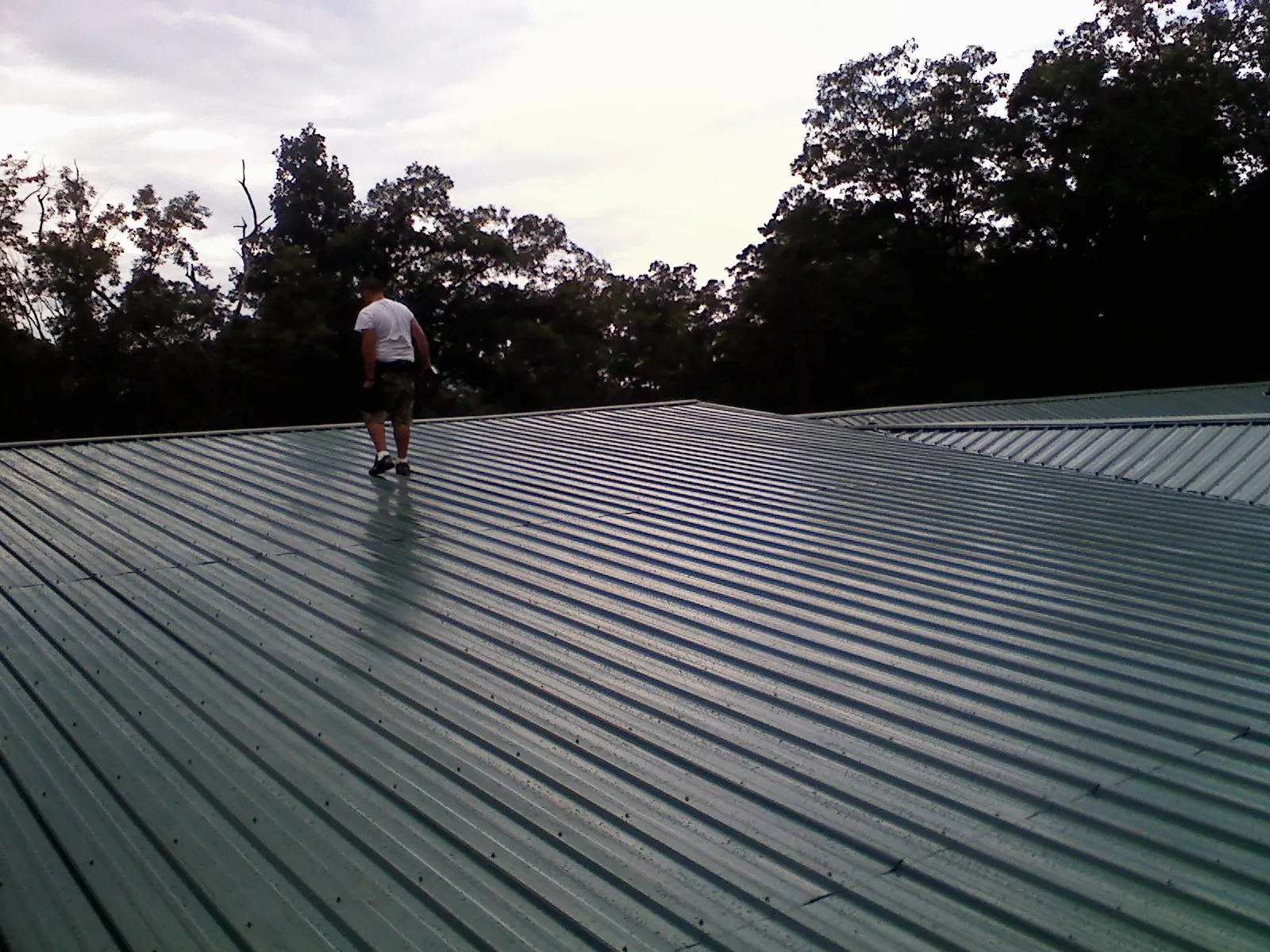 Roofer walking a wide expanse of new green metal roofing in Lake City